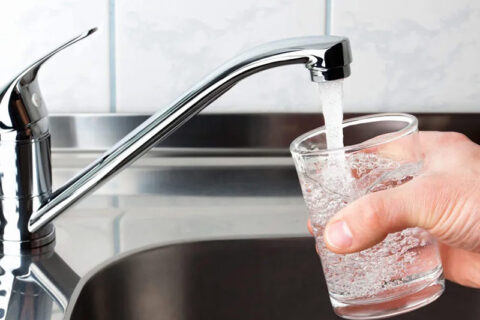 a person filling water in a glass from a tap